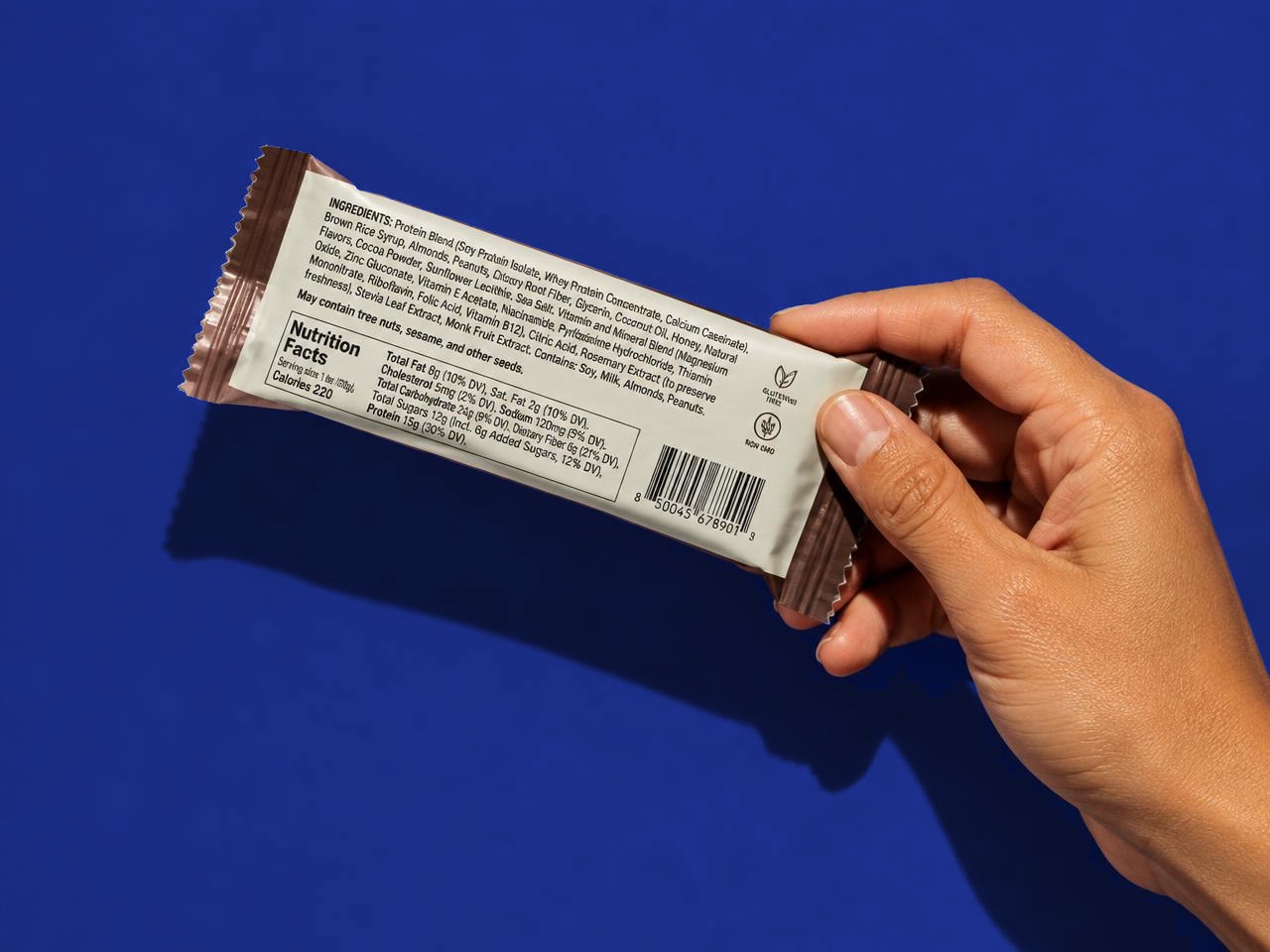 A hand turning over a conventional protein bar to reveal a long, dense ingredient list